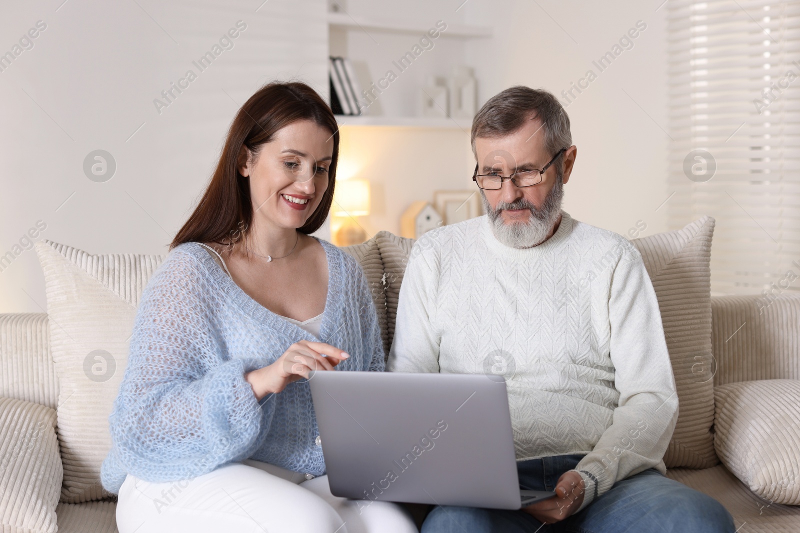 Photo of Happy daughter explaining her father how to use laptop on sofa at home