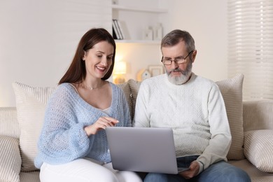 Photo of Happy daughter explaining her father how to use laptop on sofa at home