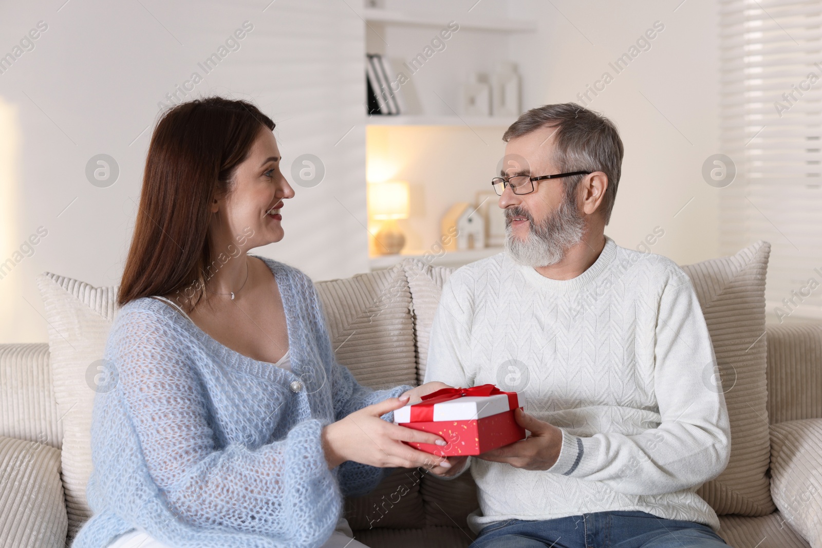 Photo of Happy daughter presenting her father with gift on sofa at home