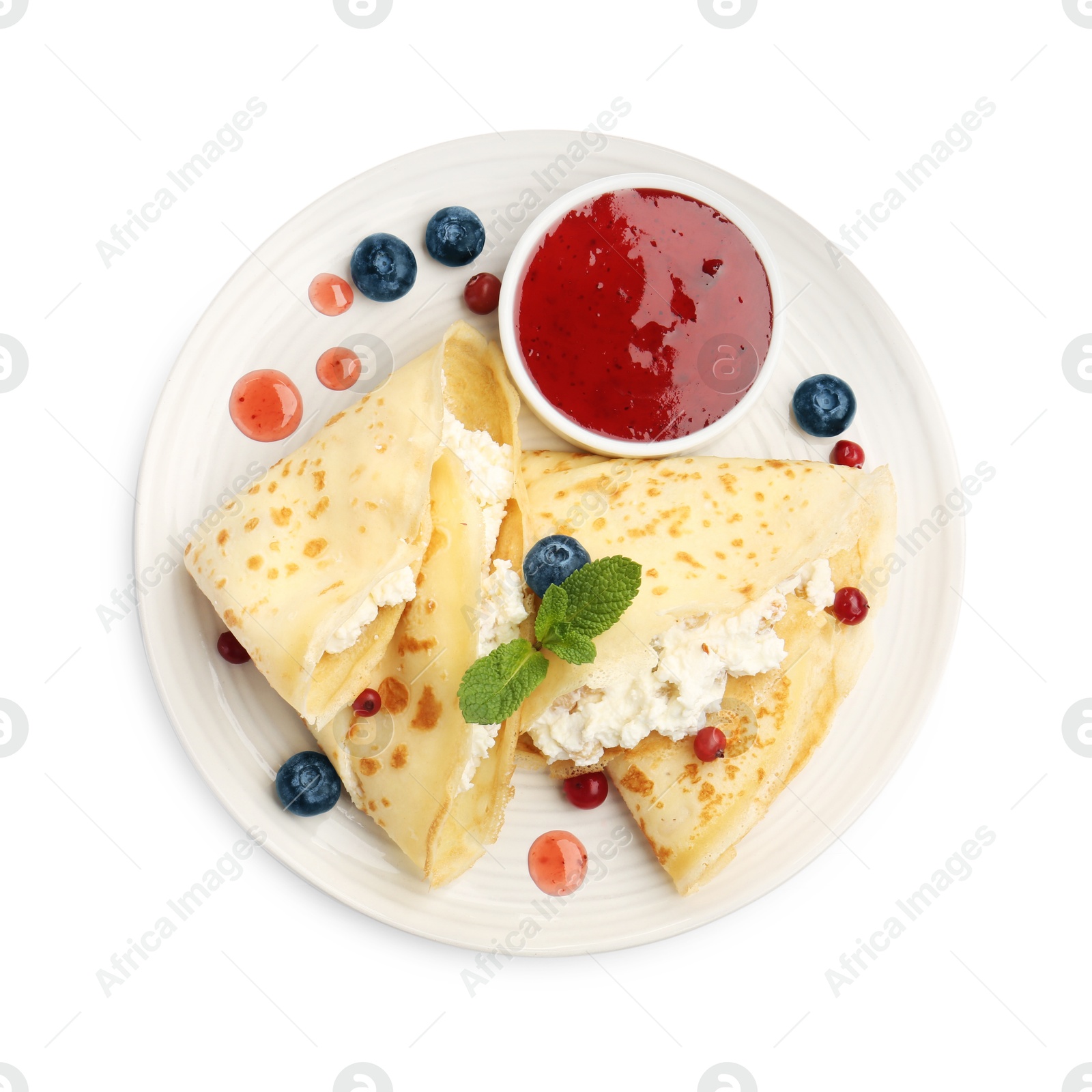 Photo of Delicious crepes with cottage cheese, jam, redcurrants and blueberries isolated on white, top view