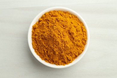 Photo of Turmeric powder in bowl on white table. Top view