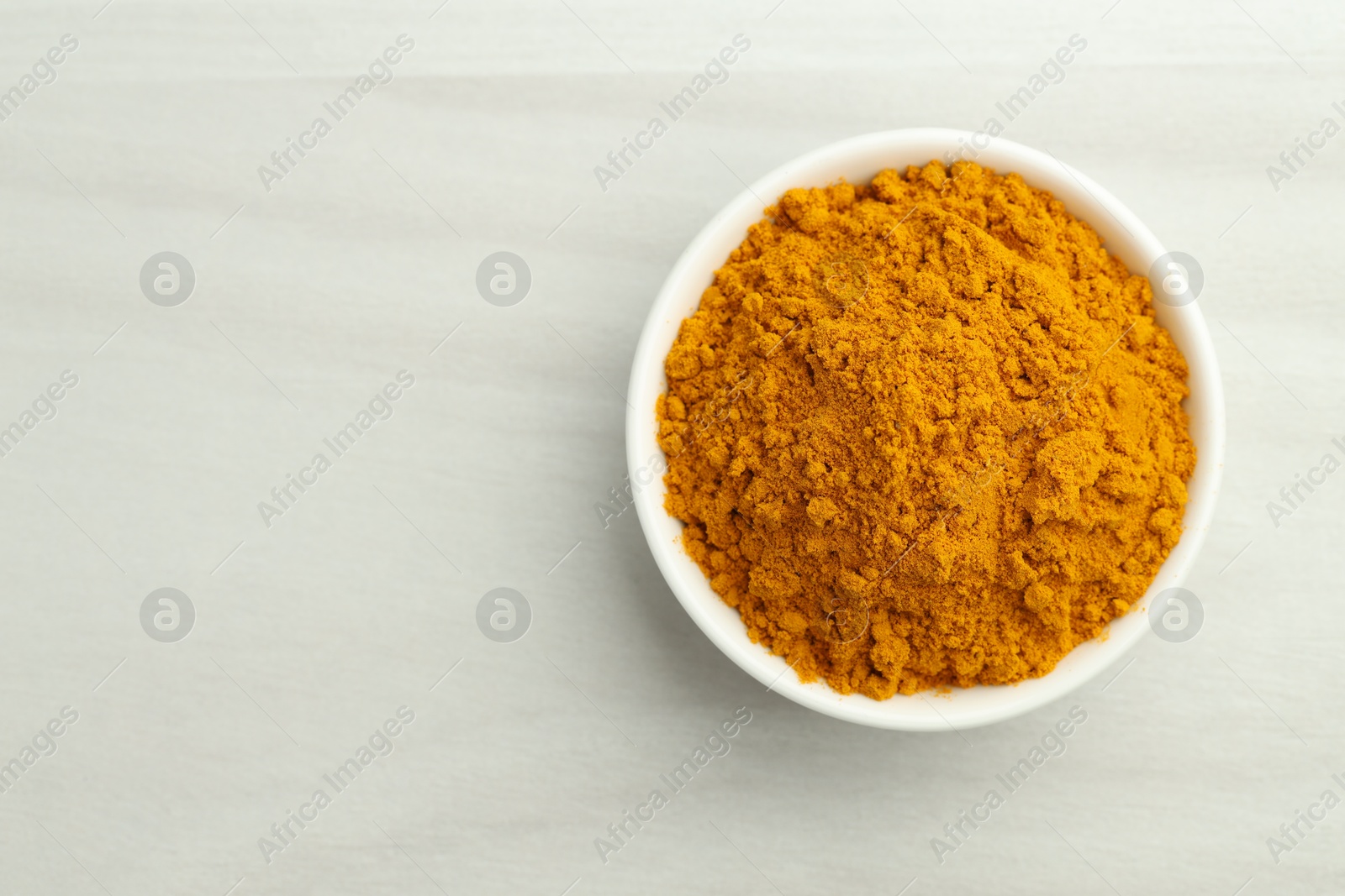 Photo of Turmeric powder in bowl on white table, top view. Space for text