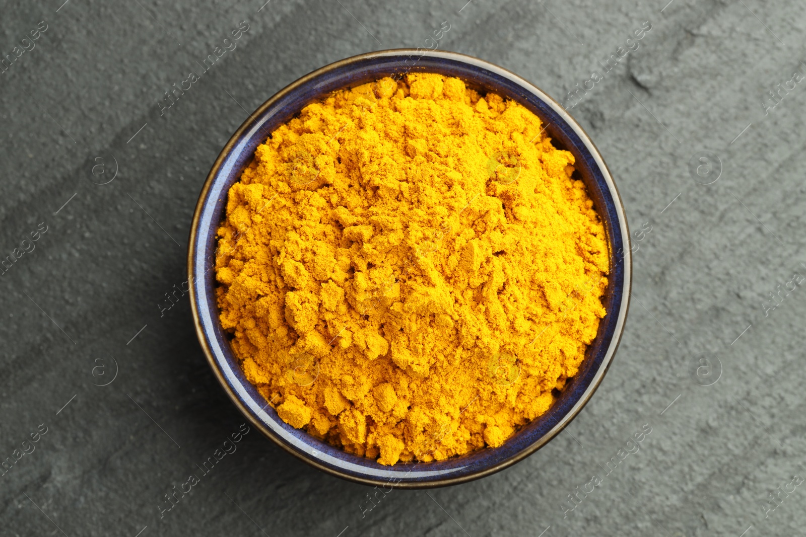 Photo of Turmeric powder in bowl on grey table, top view