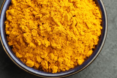 Photo of Turmeric powder in bowl on grey table, closeup. Top view