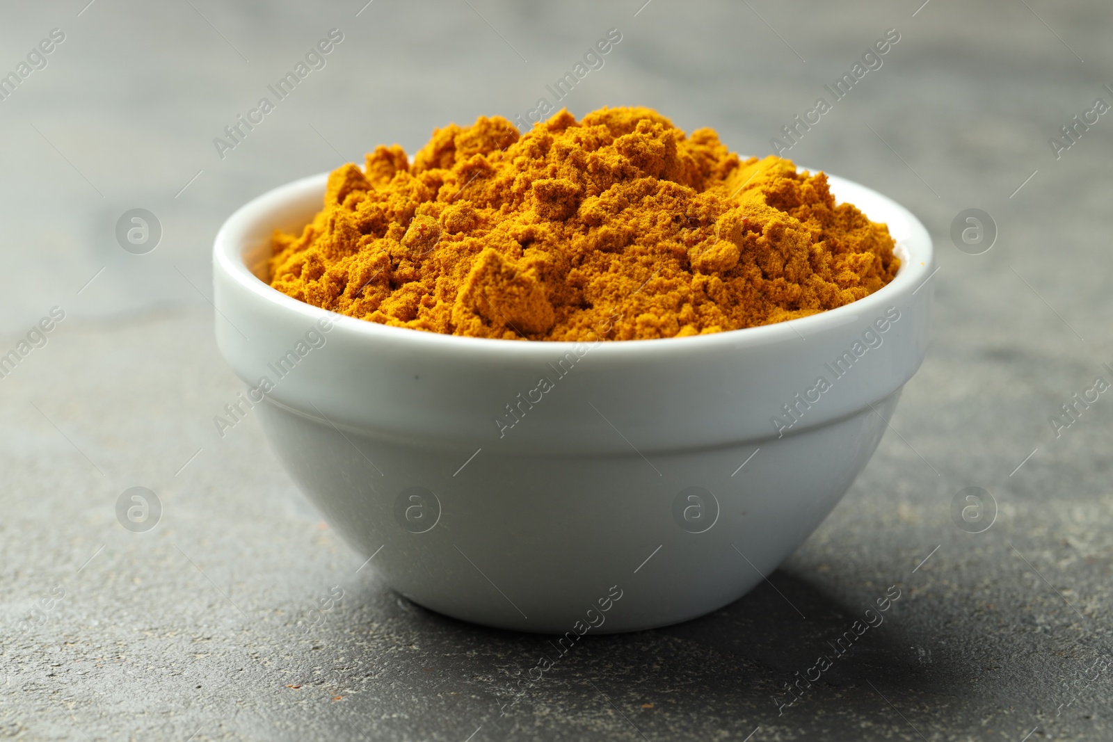 Photo of Turmeric powder in bowl on grey table, closeup