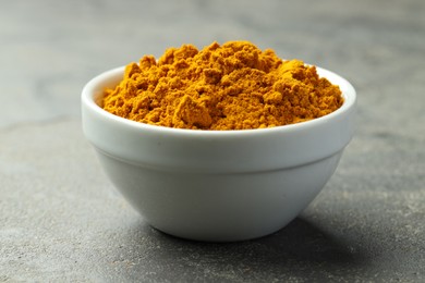 Photo of Turmeric powder in bowl on grey table, closeup