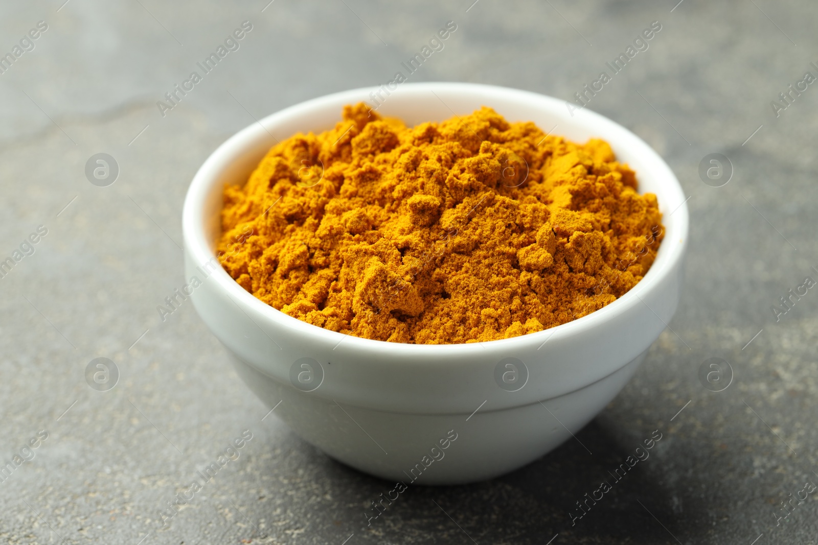 Photo of Turmeric powder in bowl on grey table, closeup