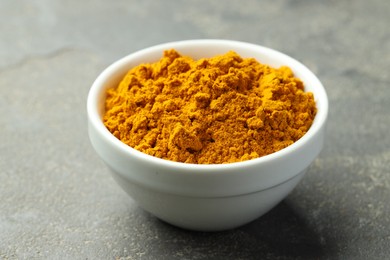 Photo of Turmeric powder in bowl on grey table, closeup