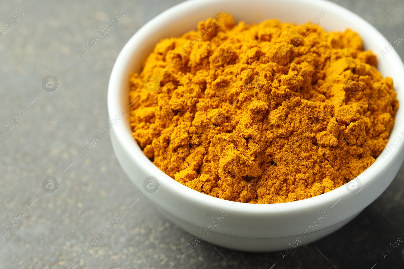 Photo of Turmeric powder in bowl on grey table, closeup