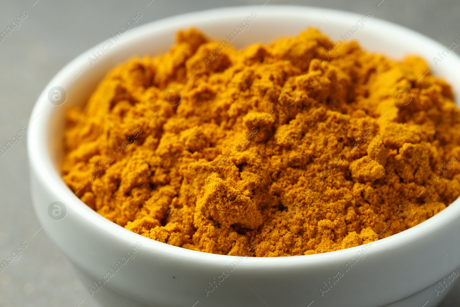 Photo of Turmeric powder in bowl on grey table, closeup