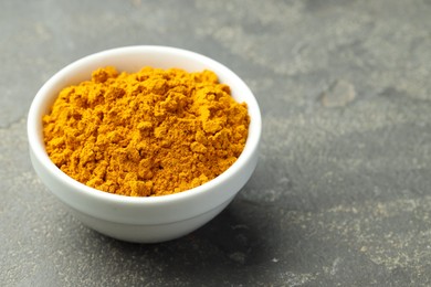 Photo of Turmeric powder in bowl on grey table, closeup. Space for text