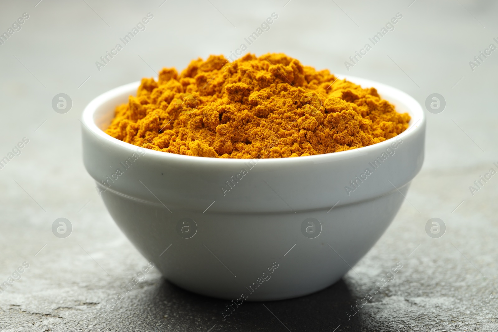 Photo of Turmeric powder in bowl on grey table, closeup