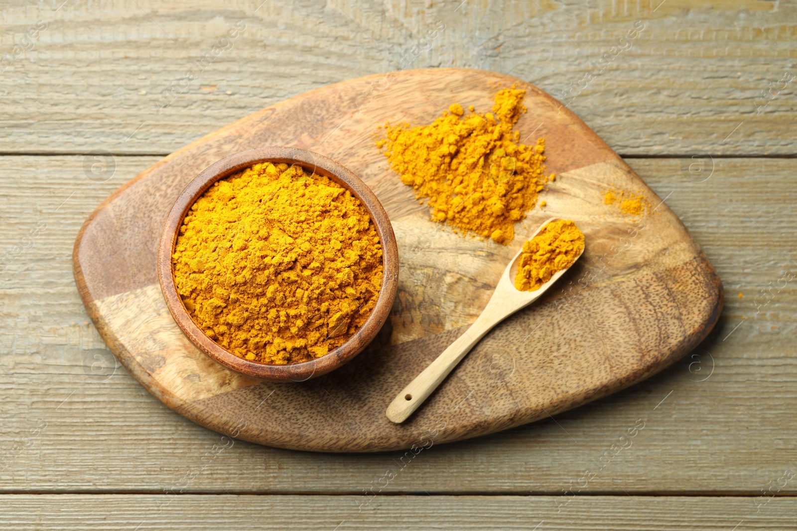 Photo of Turmeric powder in bowl and spoon on wooden table, top view