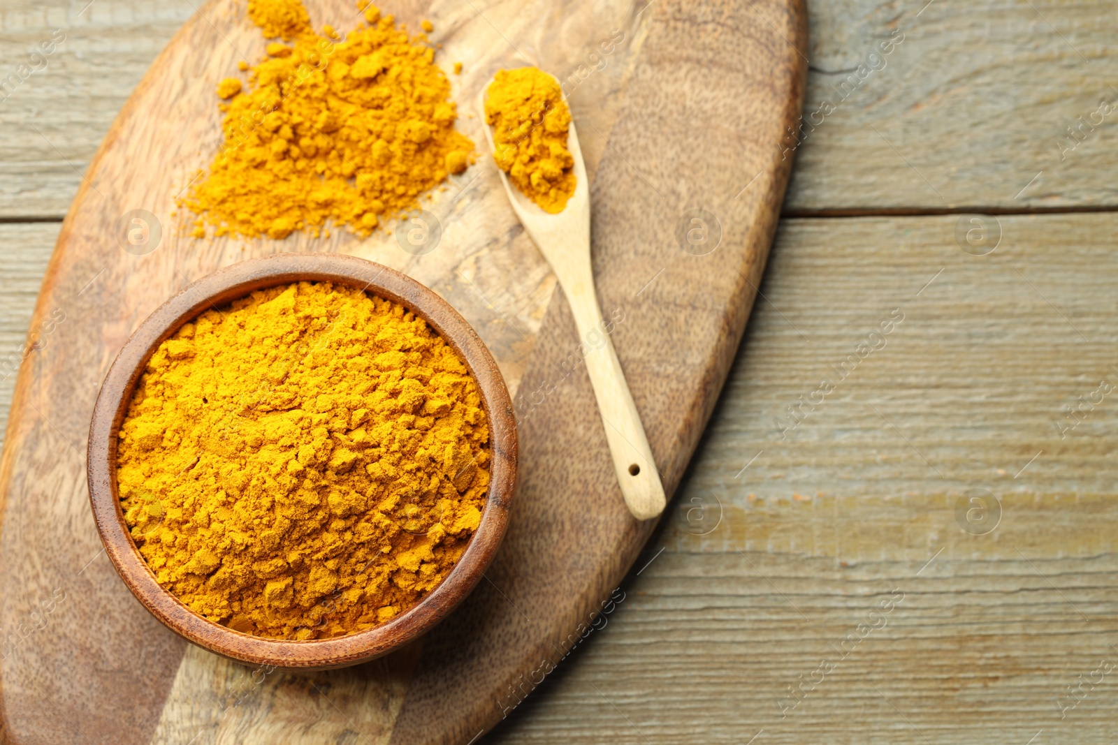 Photo of Turmeric powder in bowl and spoon on wooden table, top view. Space for text