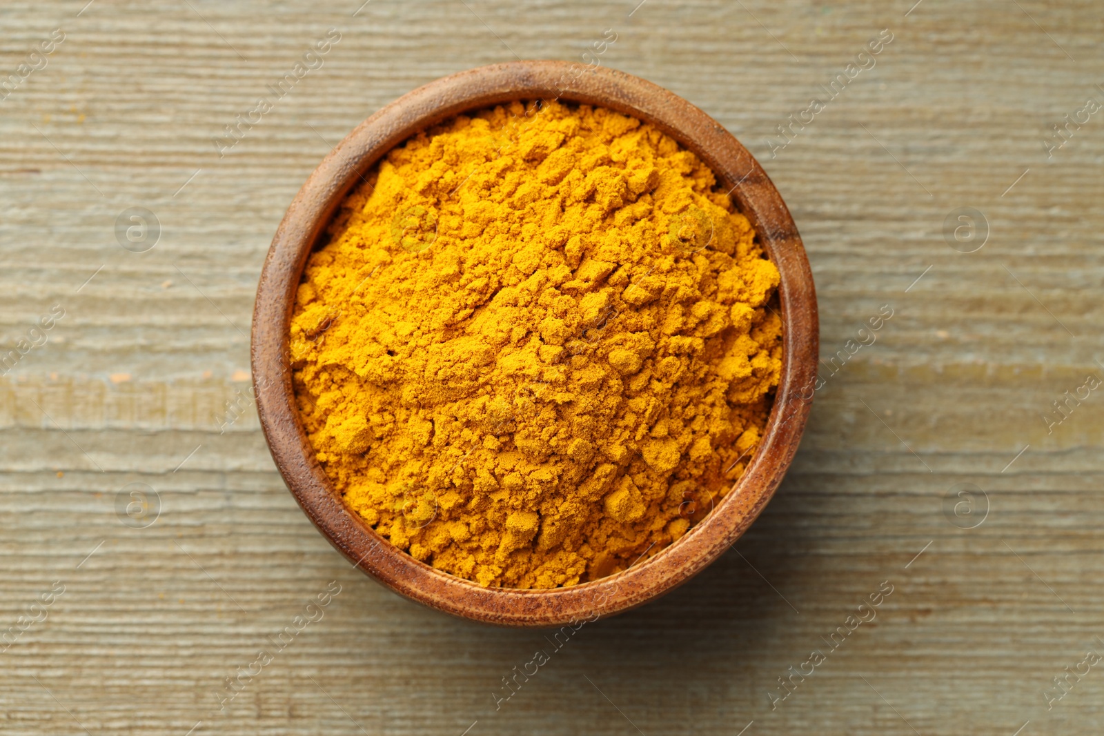 Photo of Turmeric powder in bowl on wooden table, top view