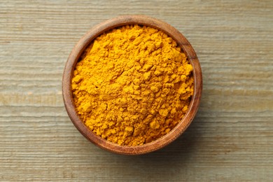 Photo of Turmeric powder in bowl on wooden table, top view