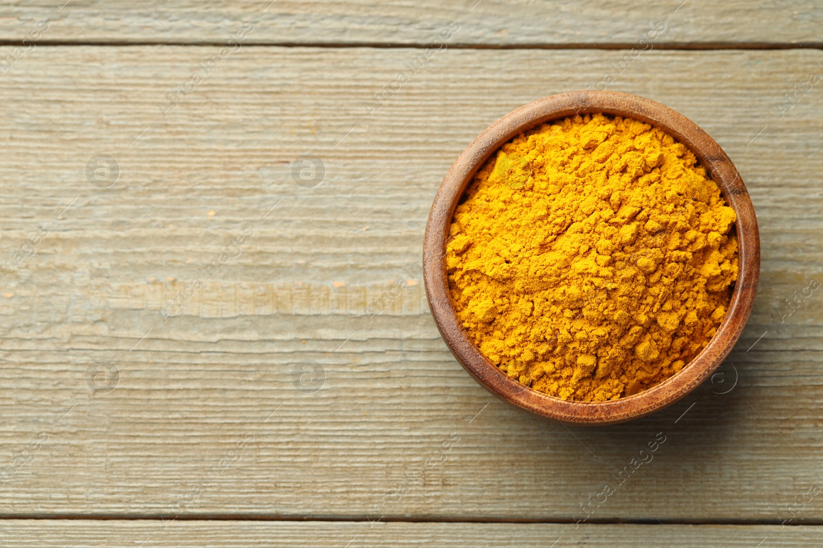 Photo of Turmeric powder in bowl on wooden table, top view. Space for text