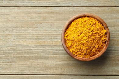 Photo of Turmeric powder in bowl on wooden table, top view. Space for text