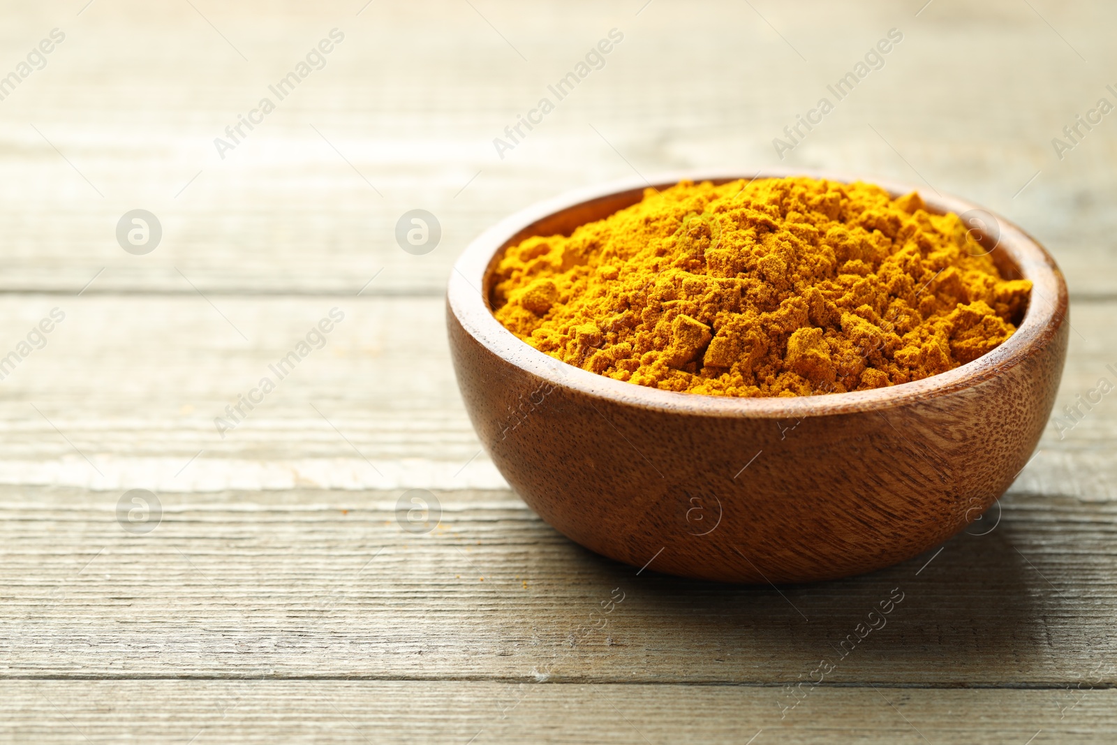 Photo of Turmeric powder in bowl on wooden table, closeup. Space for text