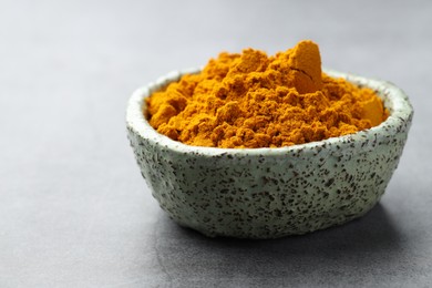 Photo of Turmeric powder in bowl on grey table, closeup