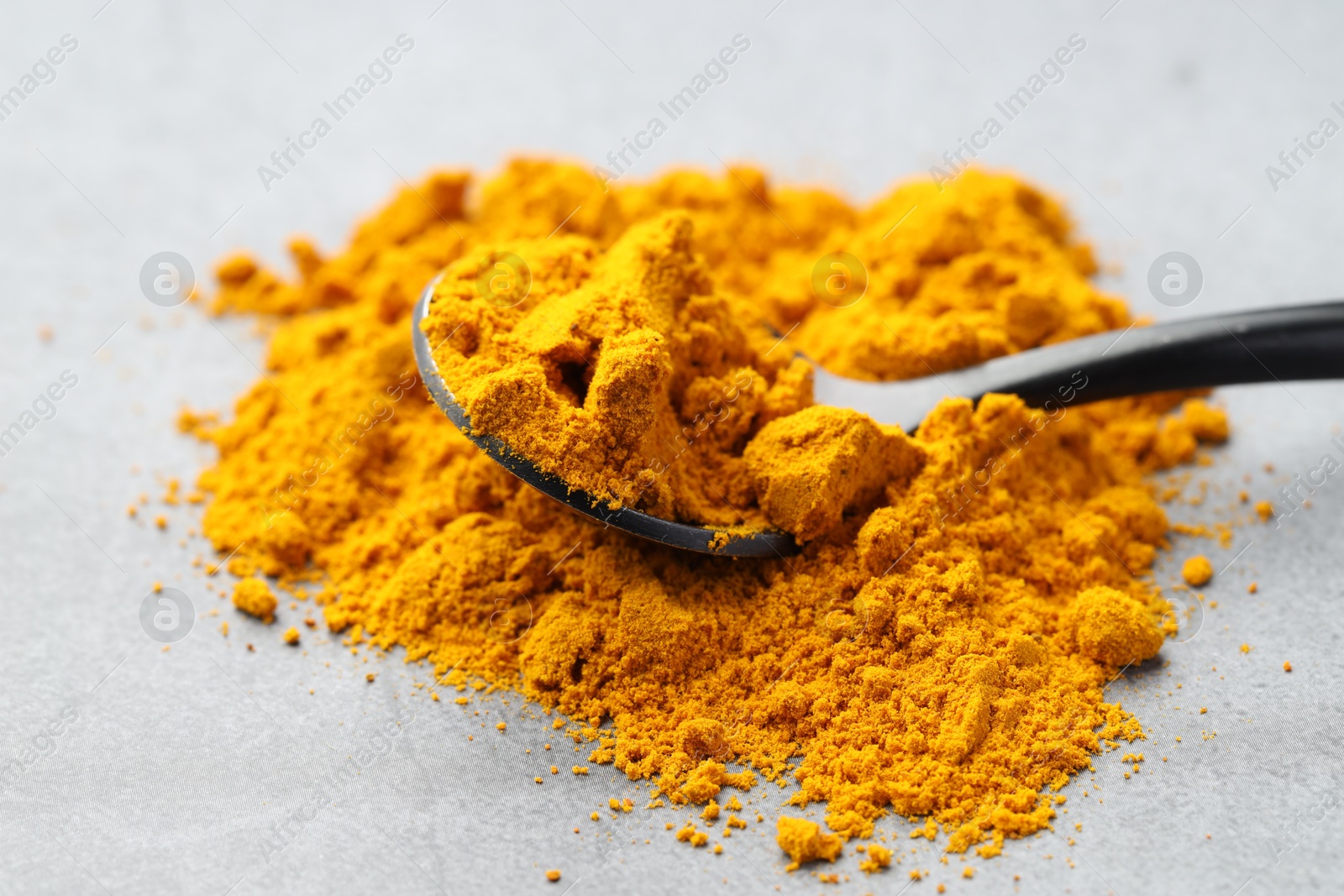 Photo of Turmeric powder and spoon on grey table, closeup