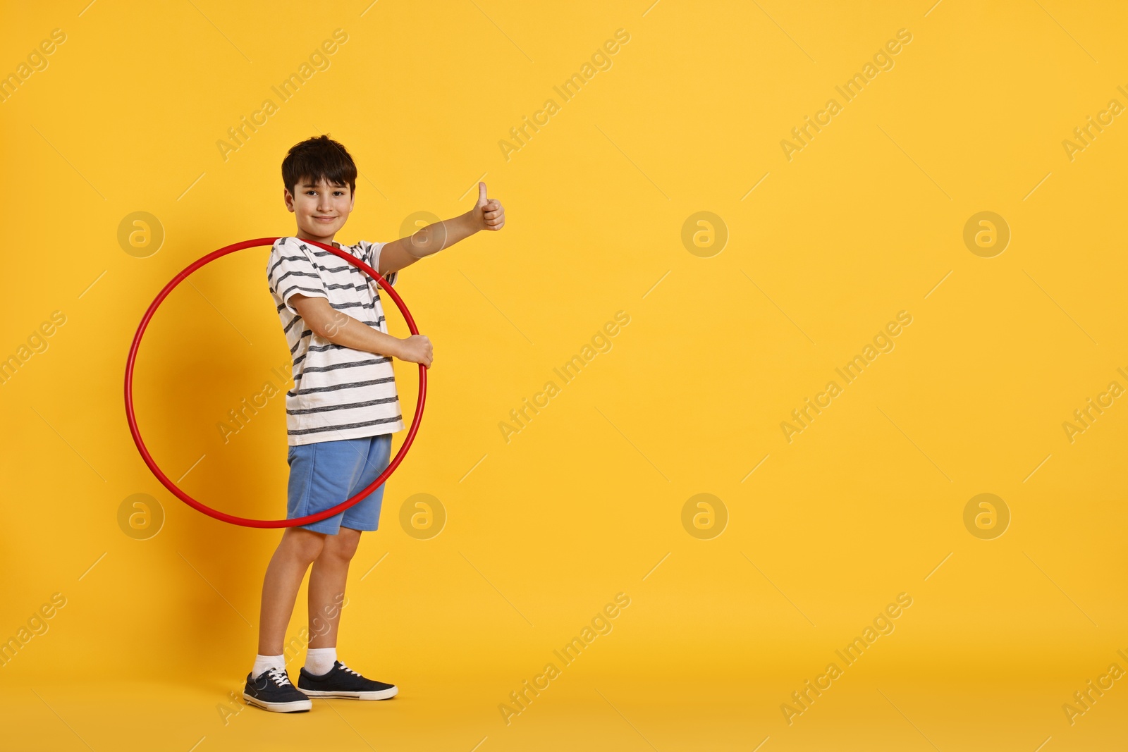 Photo of Boy with hula hoop showing thumbs up on yellow background, space for text