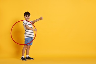 Photo of Boy with hula hoop showing thumbs up on yellow background, space for text