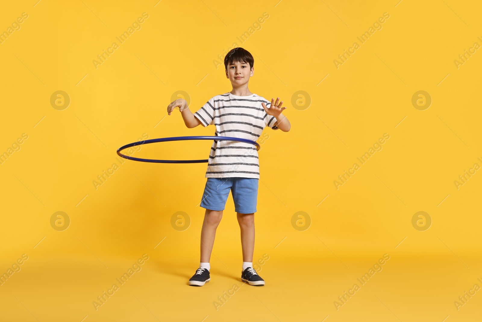 Photo of Boy exercising with hula hoop on yellow background