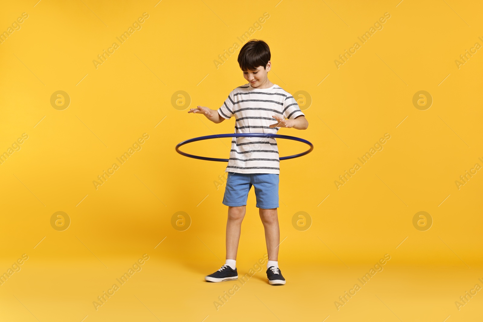 Photo of Boy exercising with hula hoop on yellow background