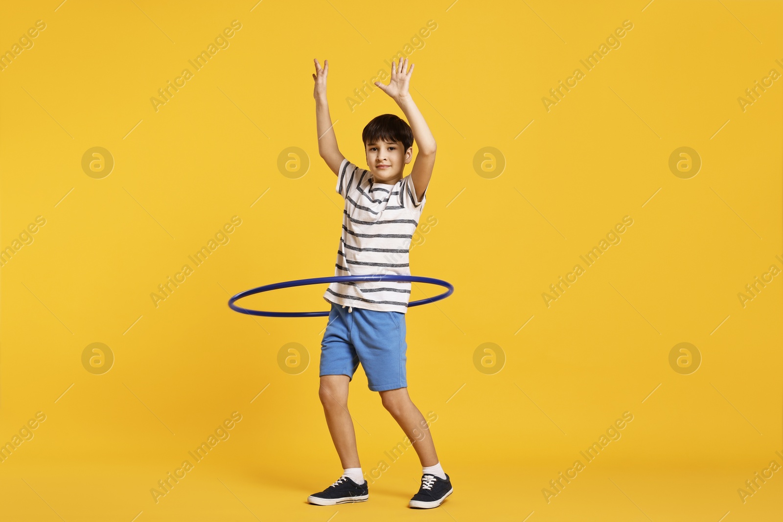 Photo of Boy exercising with hula hoop on yellow background