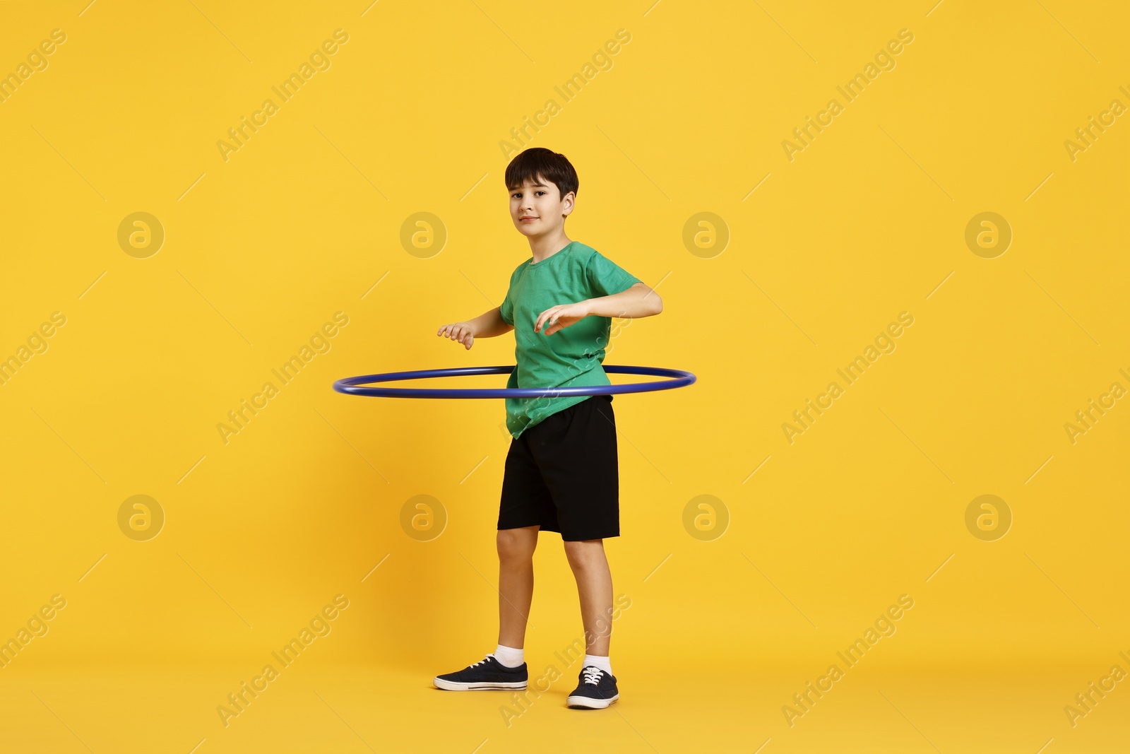 Photo of Boy exercising with hula hoop on yellow background