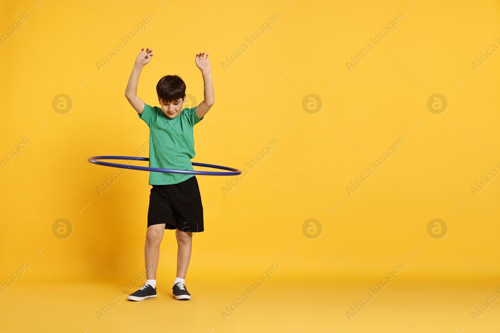 Photo of Boy exercising with hula hoop on yellow background, space for text