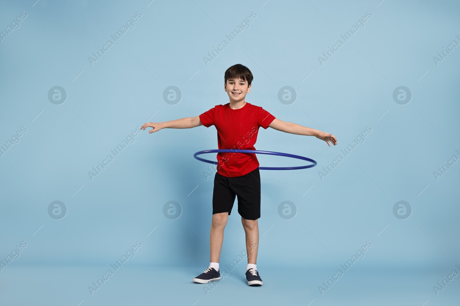 Photo of Smiling boy exercising with hula hoop on light blue background