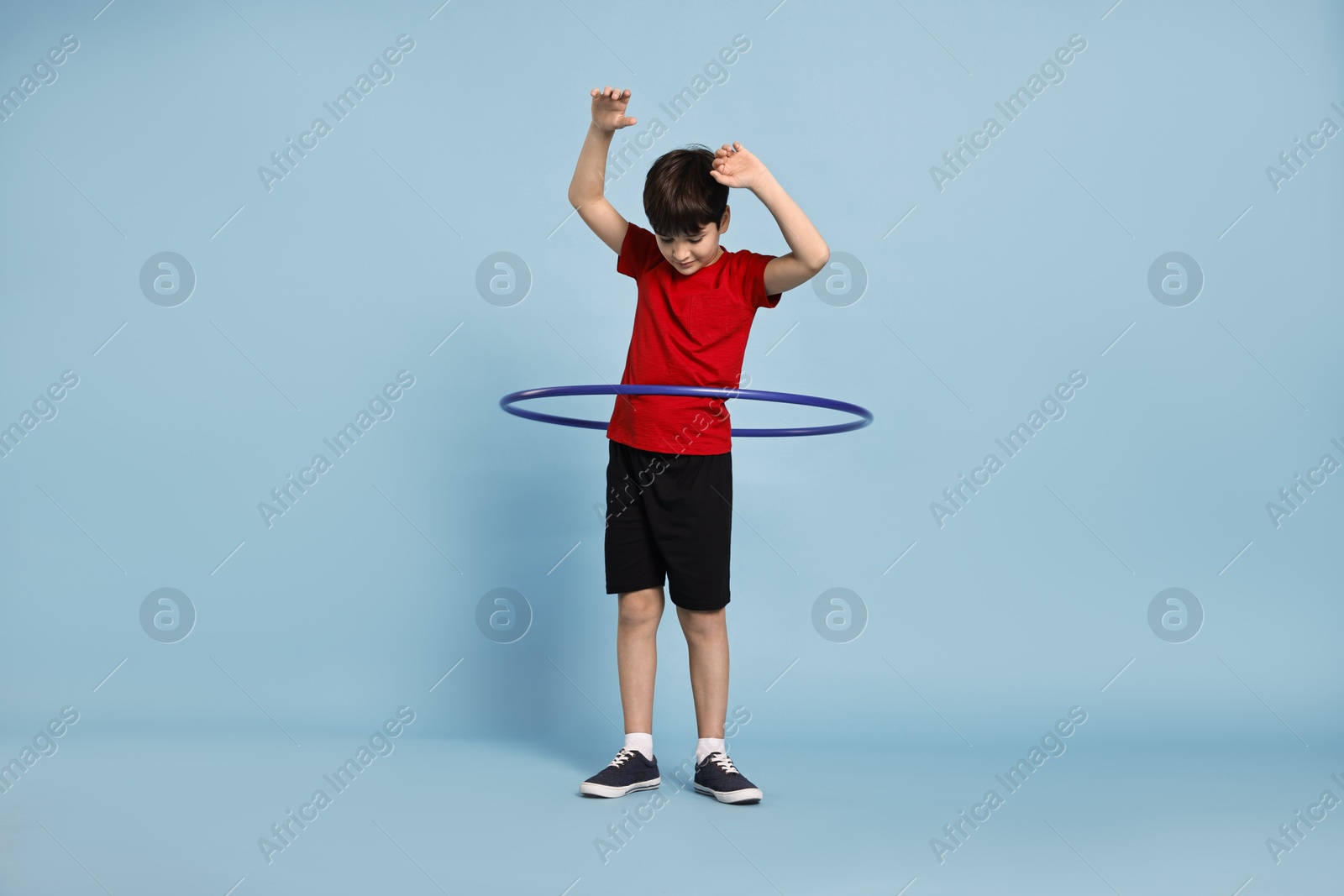 Photo of Boy exercising with hula hoop on light blue background