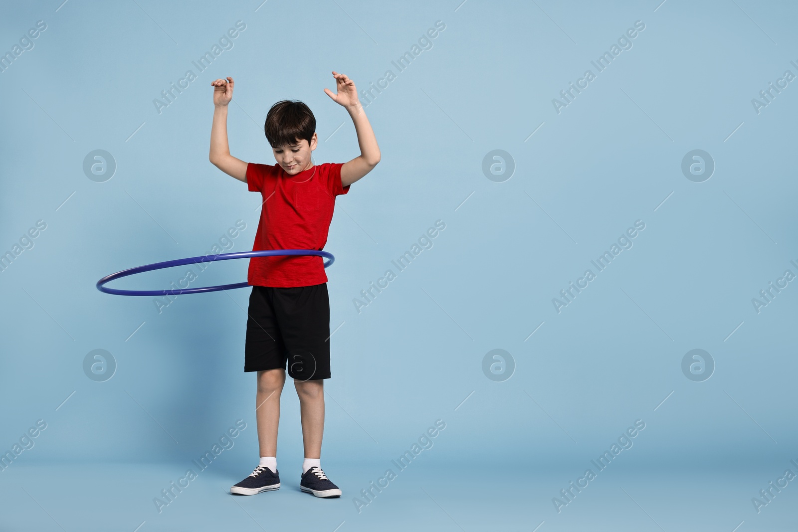 Photo of Boy exercising with hula hoop on light blue background, space for text