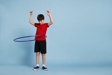 Photo of Boy exercising with hula hoop on light blue background, space for text