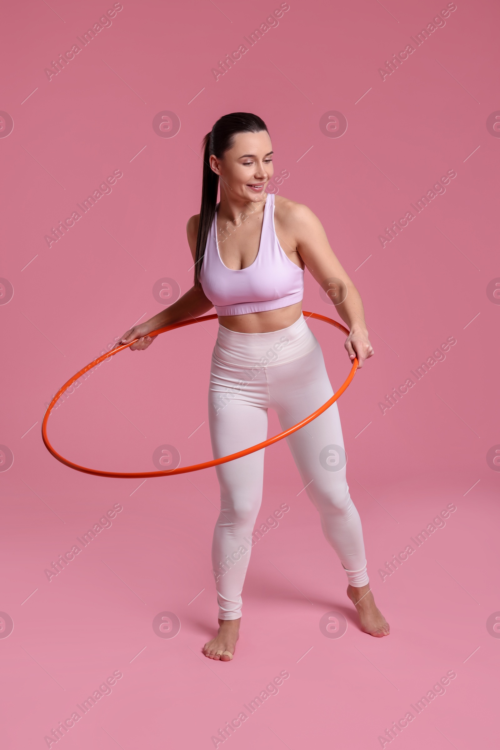 Photo of Smiling woman training with hula hoop on pink background