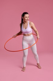 Photo of Smiling woman training with hula hoop on pink background