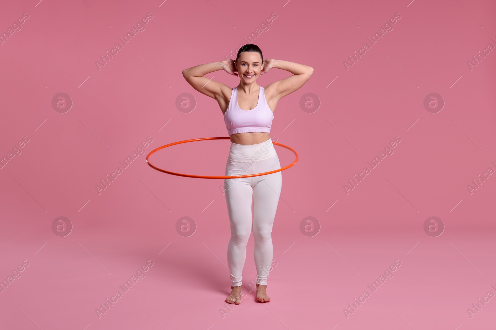 Photo of Smiling woman training with hula hoop on pink background