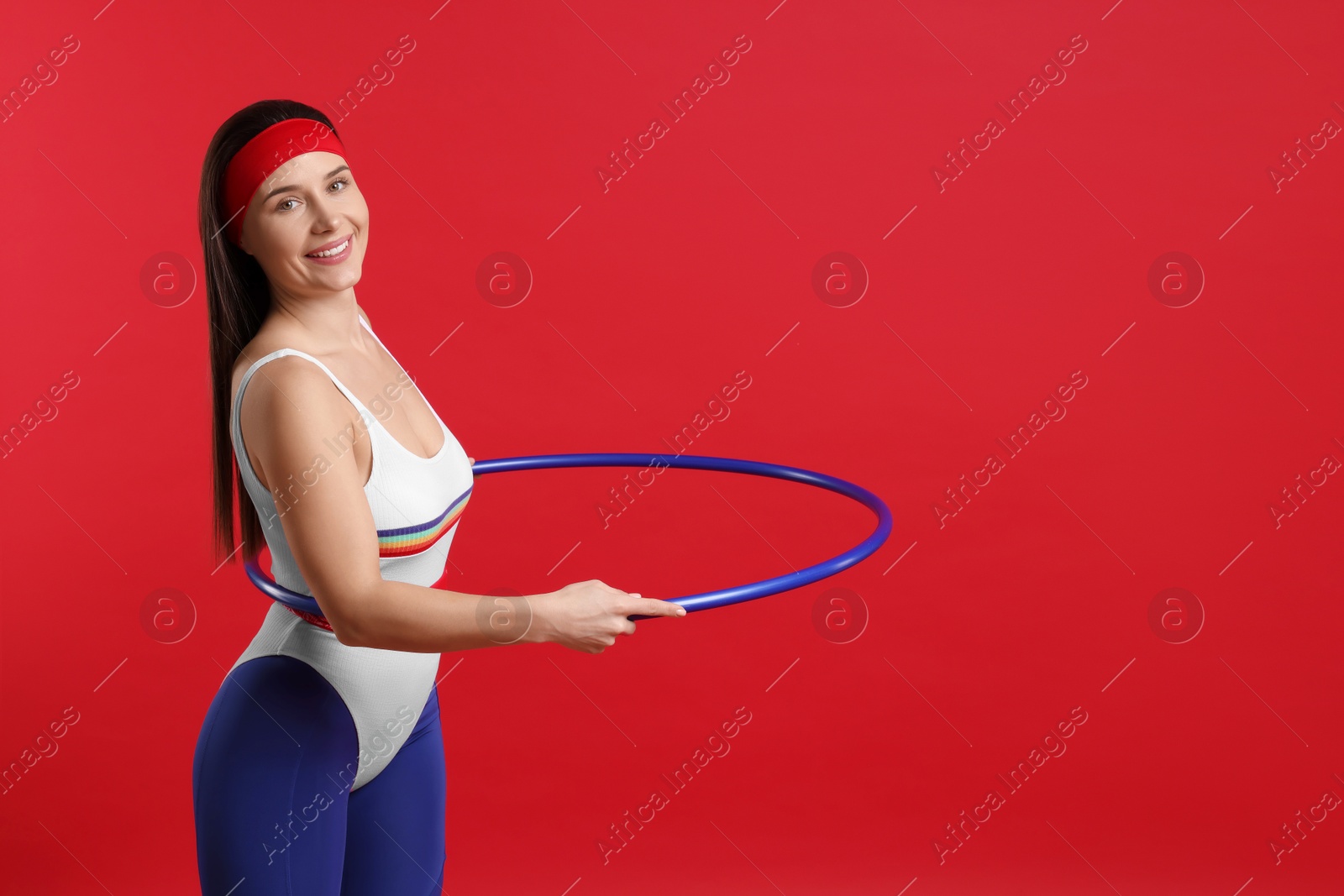 Photo of Smiling woman training with hula hoop on red background. Space for text