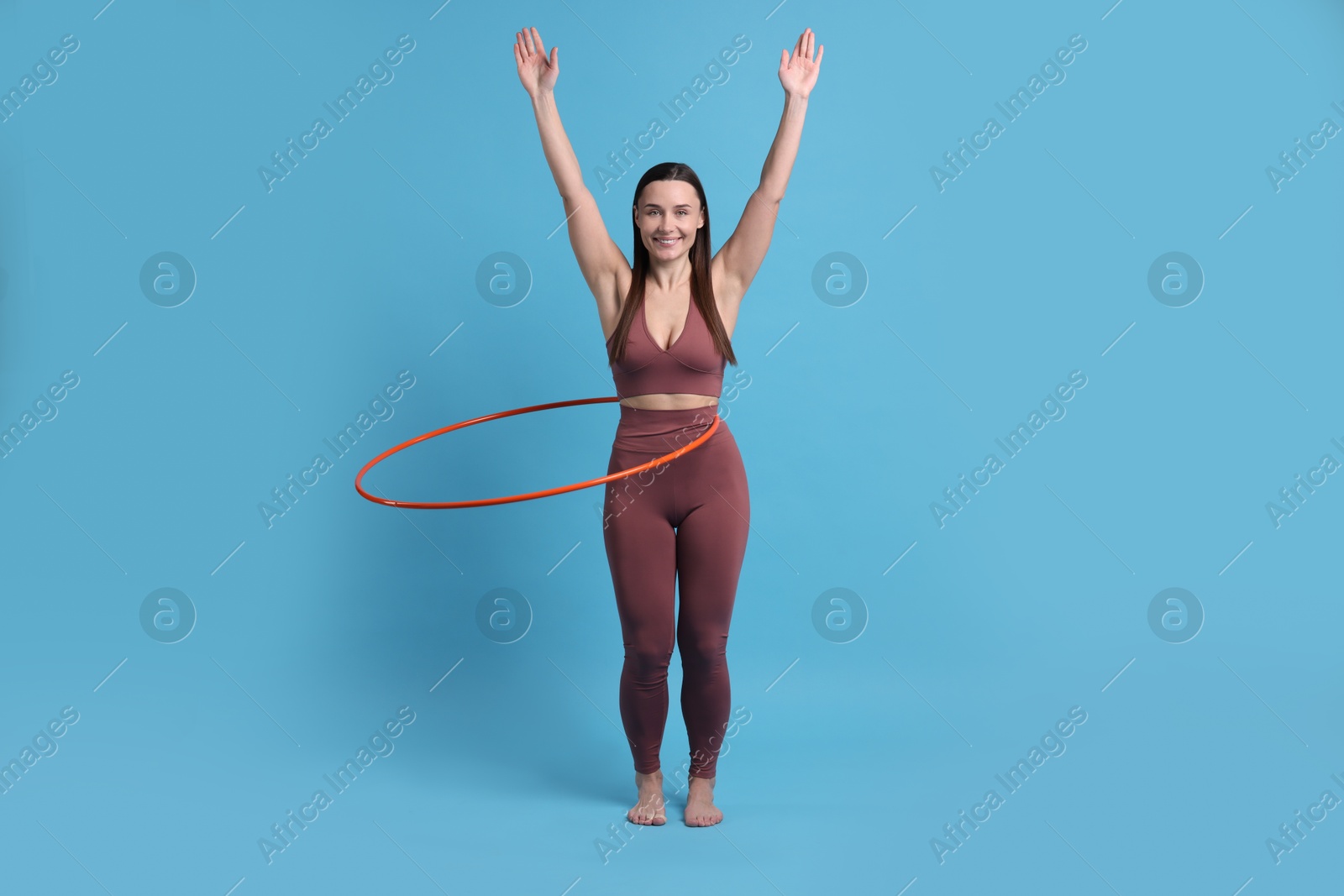 Photo of Smiling woman training with hula hoop on light blue background