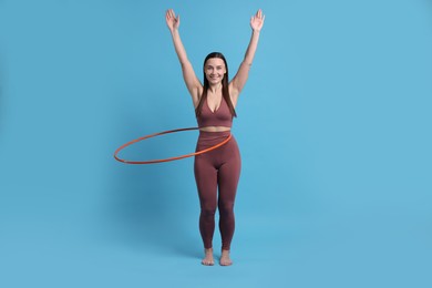 Photo of Smiling woman training with hula hoop on light blue background