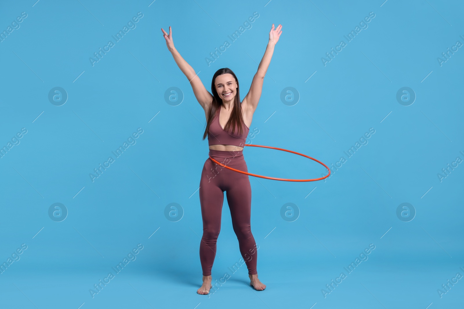 Photo of Smiling woman training with hula hoop on light blue background