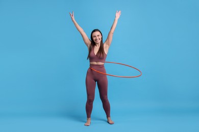 Photo of Smiling woman training with hula hoop on light blue background