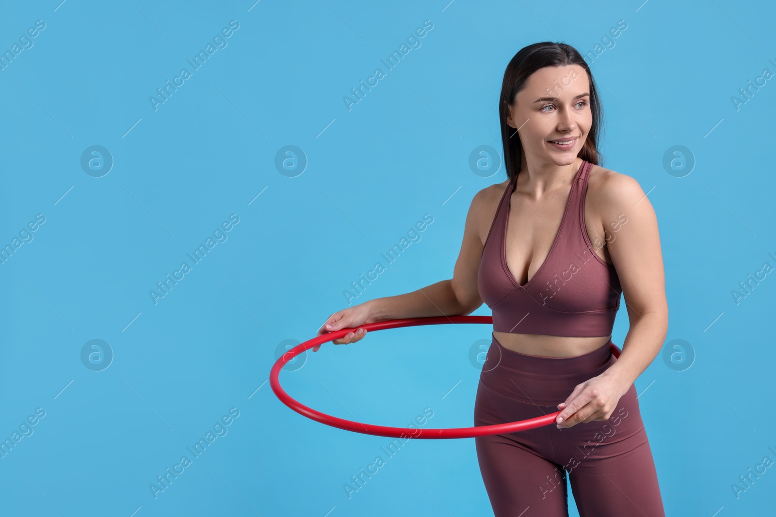 Photo of Smiling woman training with hula hoop on light blue background. Space for text