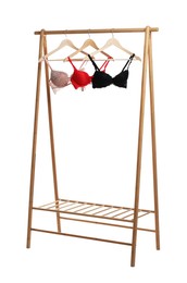 Photo of Hangers with beautiful bras on wooden rack against white background