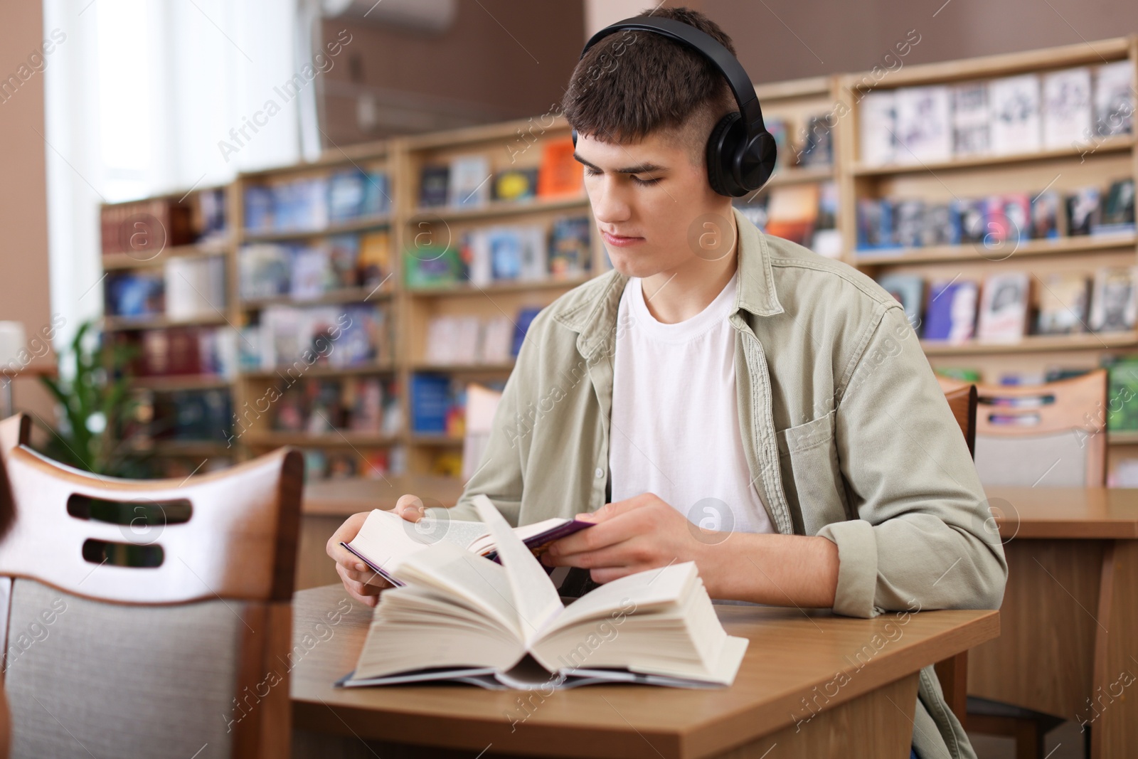 Photo of Man in headphones reading books at desk in public library