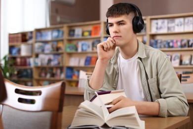 Photo of Man in headphones with books at desk in public library