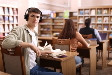 Photo of Man in headphones with books at desk in public library