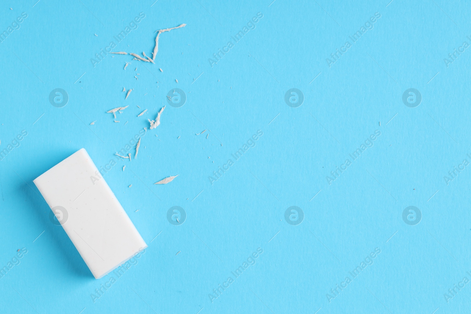 Photo of One eraser and scraps on light blue background, top view. Space for text